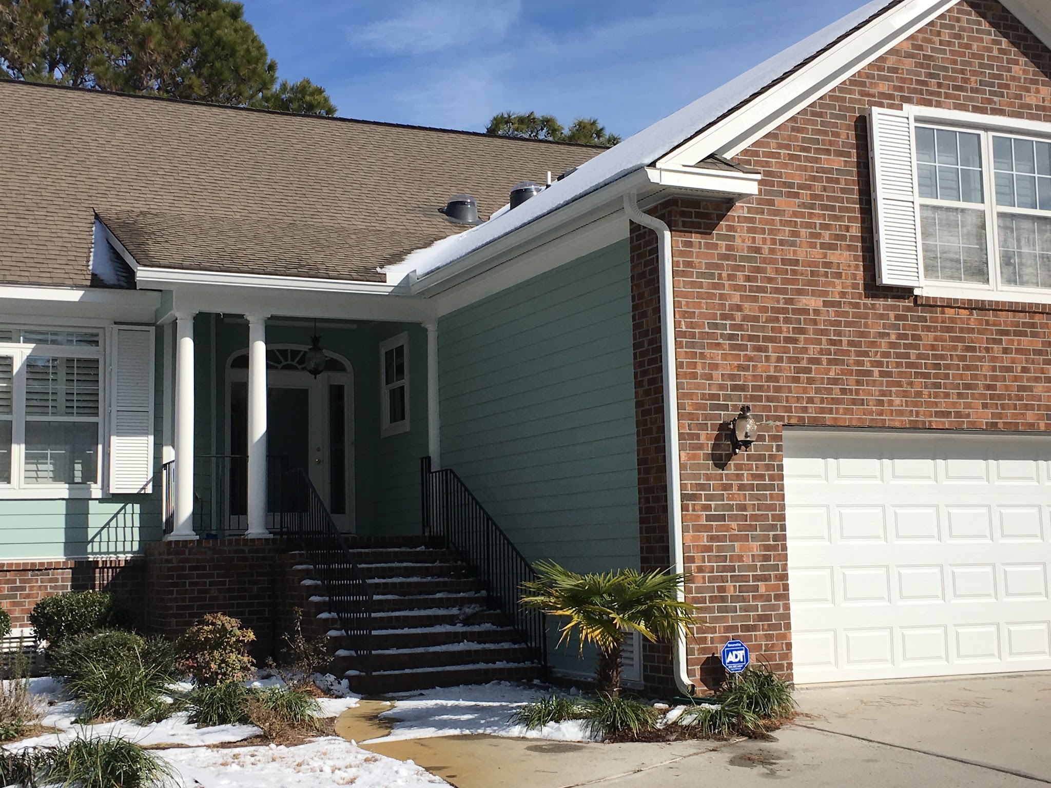 Brick and green-sided home with white seamless gutters